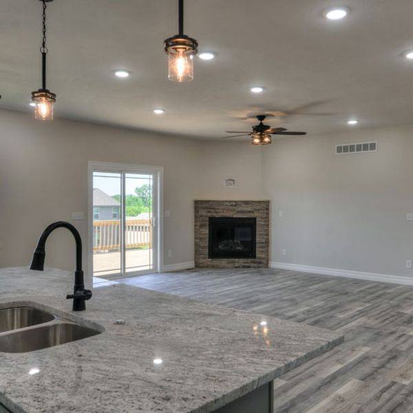 Open living room with a fireplace, ceiling fans and grey granite counters.