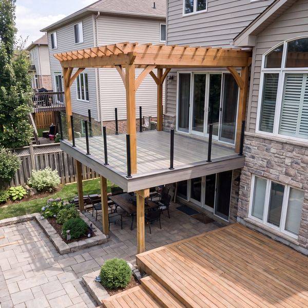 Backyard deck with a timber pergola, glass railing and stone-clad house.