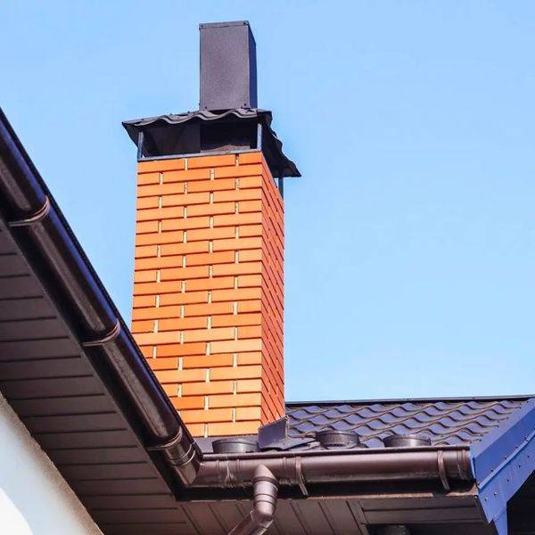 Tall orange brick chimney with a black cap on a blue-sky day.