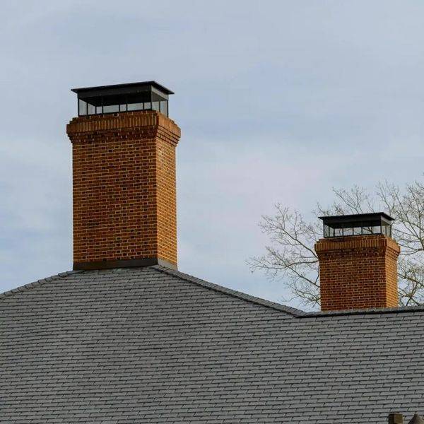 Two brick chimneys with black metal caps rising above a shingled roof.