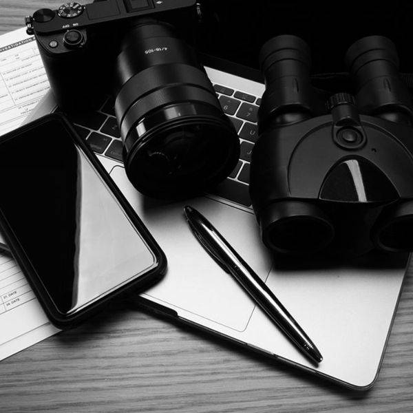 Binoculars, a phone and a pen on a notepad on a desk.