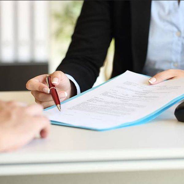 A hand holds a pen over a document on a desk.