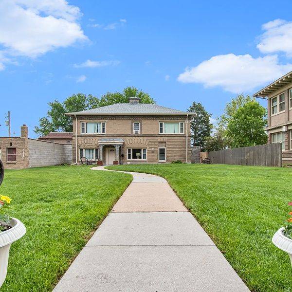 Front walk leading to a two-story house, flanked by flower planters and a lawn.