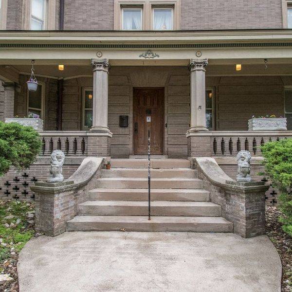 Front porch and stone steps of a large brick house with columns and a wooden door.
