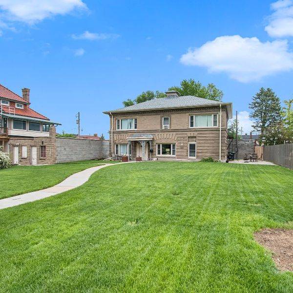 Brick house with a red roof and a sloped lawn on a sunny street.