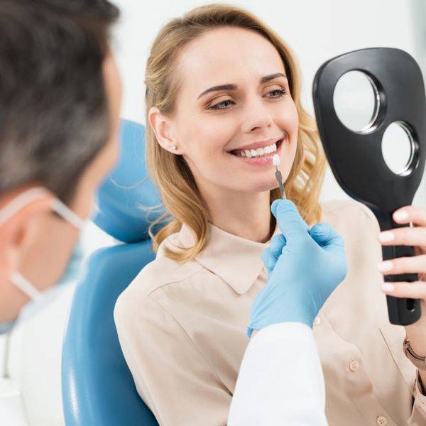 Smiling woman holding a dark dental device while a dentist in gloves works nearby