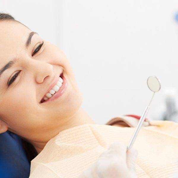 Smiling patient reclining in a dental chair with a mirror nearby