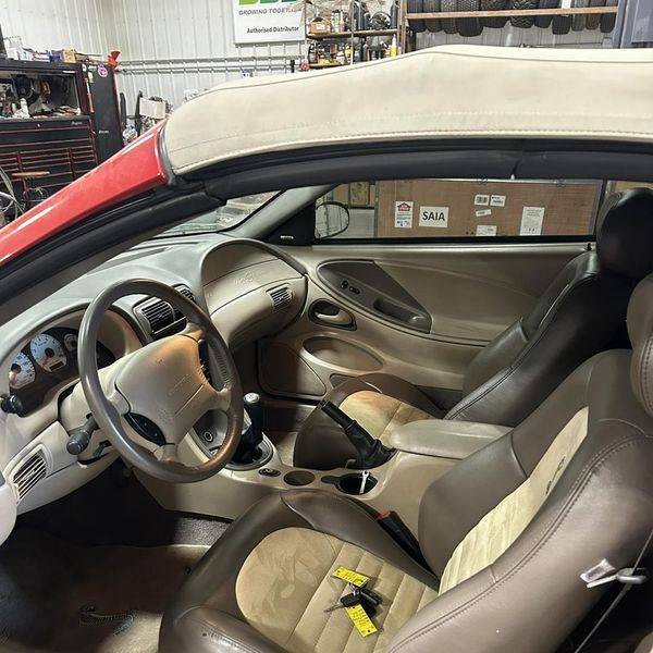Interior of a Mustang showing the dashboard, steering wheel and tan seats.