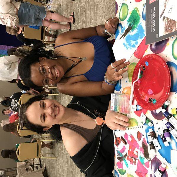 Group of people smiling together around a colorful painting table during an art session.