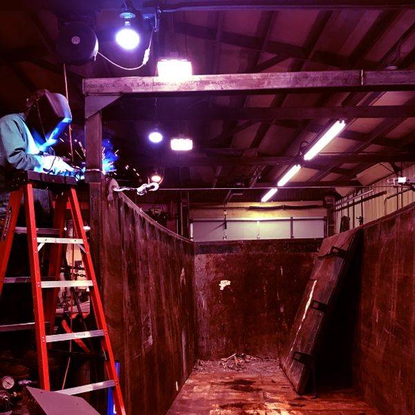 Welder working inside a dark fabrication pit under bright work lights