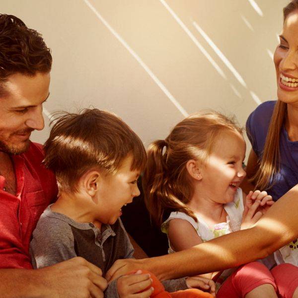 Smiling parents with two young children sitting together indoors in warm light.