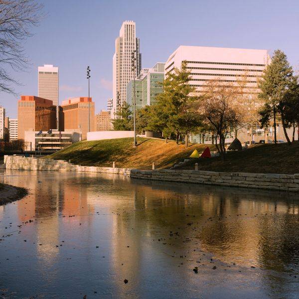 City skyline seen across a pond with trees and buildings in warm light.