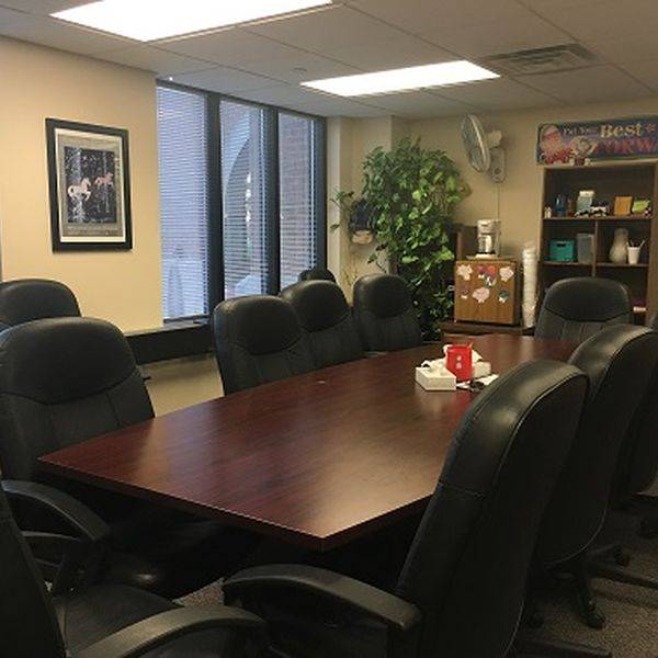 Conference room with a long wood table and black chairs by windows.