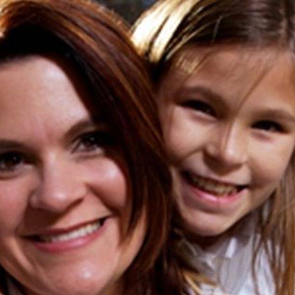 Smiling woman and a young girl posing close together, both looking at the camera.