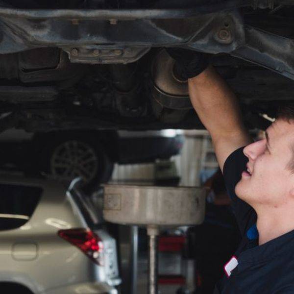 A mechanic working underneath a raised car in a shop.