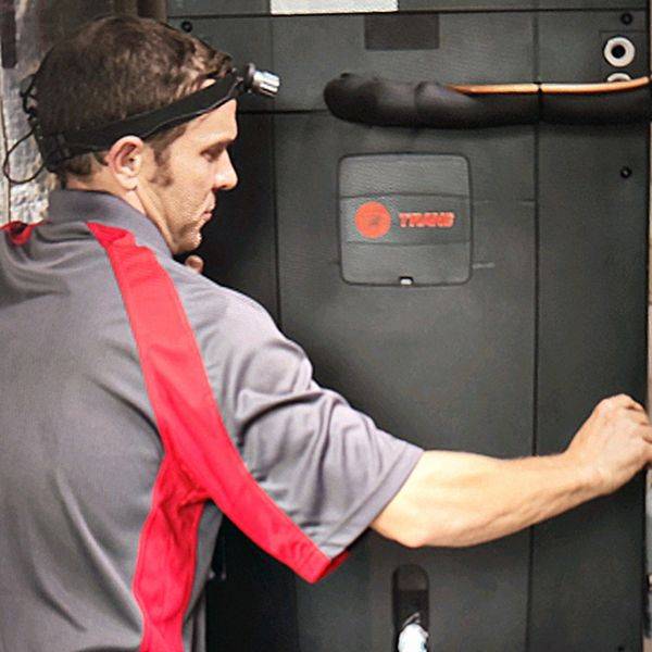 Technician in a red-striped shirt working on a dark furnace unit.