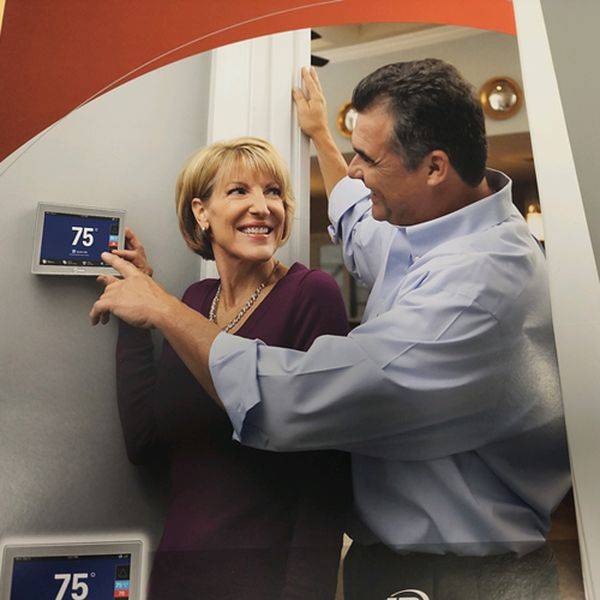 Smiling couple adjusting a wall thermostat set to 75 degrees at home.