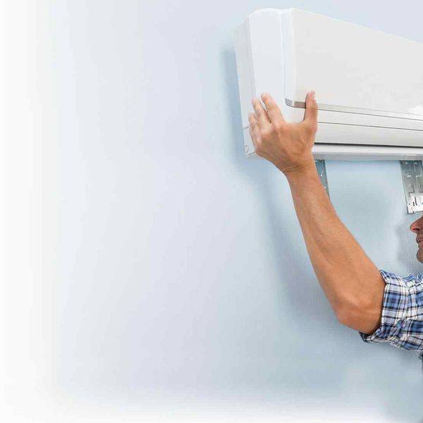 Technician mounting a wall-mounted ductless air conditioner indoors.