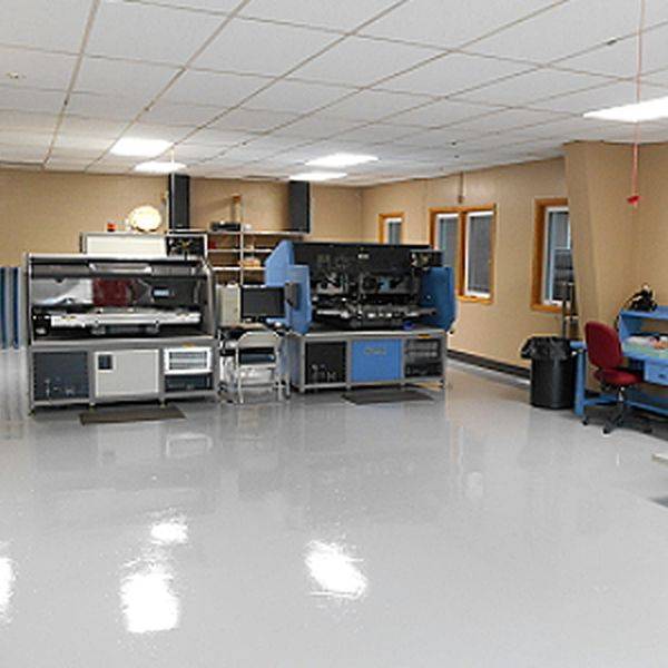 Clean electronics test lab with equipment racks, workbenches and test stations along a polished floor.