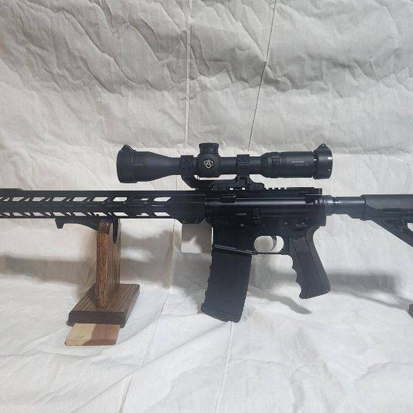 Black rifle with a scope and folding stock on a white cloth.