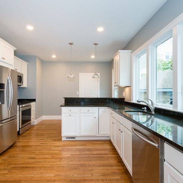 Modern kitchen with stainless steel refrigerator, white cabinets and dark granite countertops.