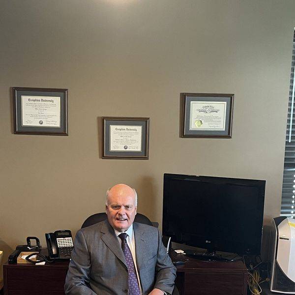 An attorney seated at his desk in an office with framed certificates on the wall.