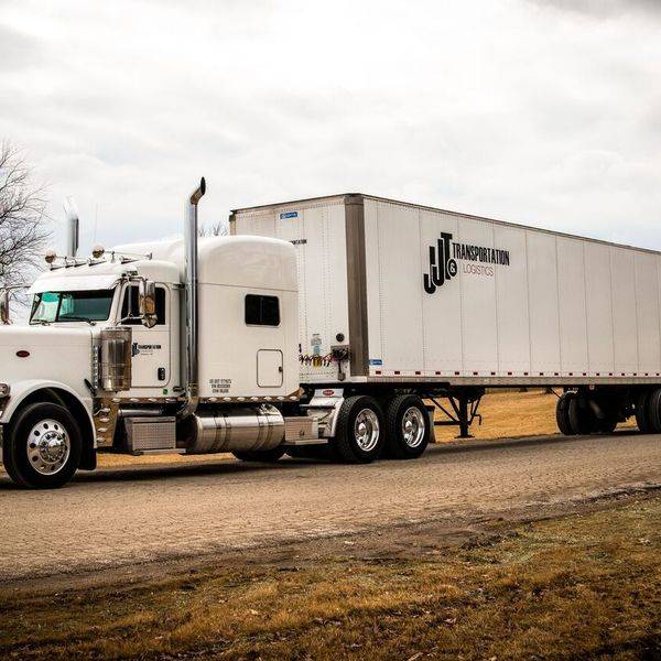 A white semi truck and long trailer with a small logo on the side, on a dry grassy hill.