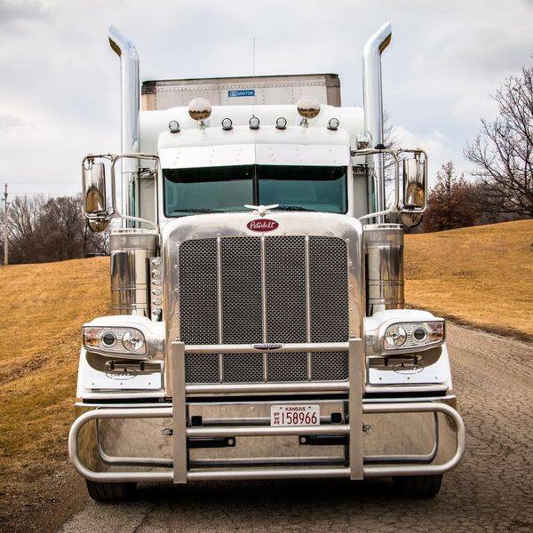 A white semi truck with a chrome grille and bumper, parked on a grassy rise.