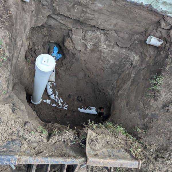 A dug trench exposing a white pipe and a blue valve for underground water service.