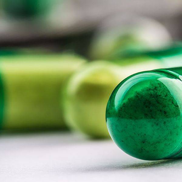 Glossy green capsules lie on a light surface in a close-up view.
