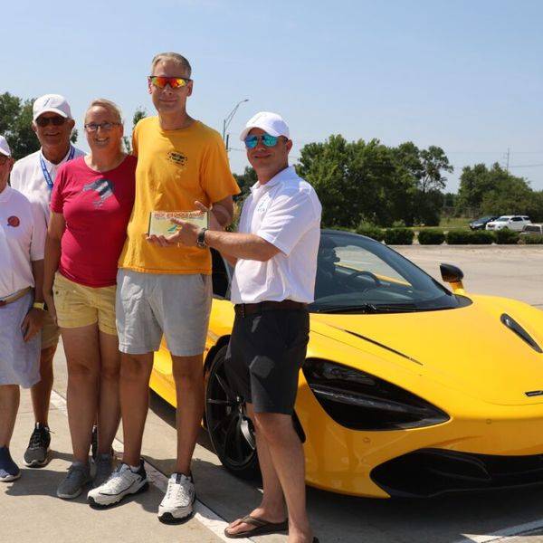 Four people posing beside a bright yellow sports car at an outdoor car show.