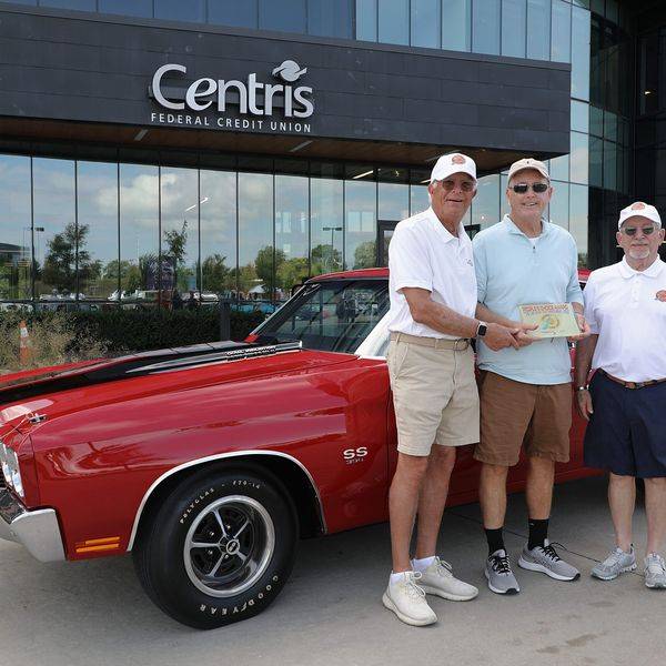 Group of men holding a certificate beside a red classic muscle car at a car show.