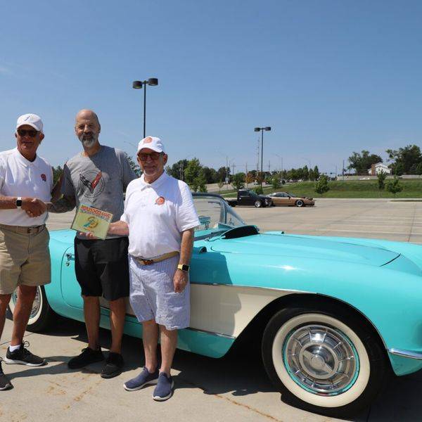 Men posing with an award beside a turquoise classic convertible in a parking lot.