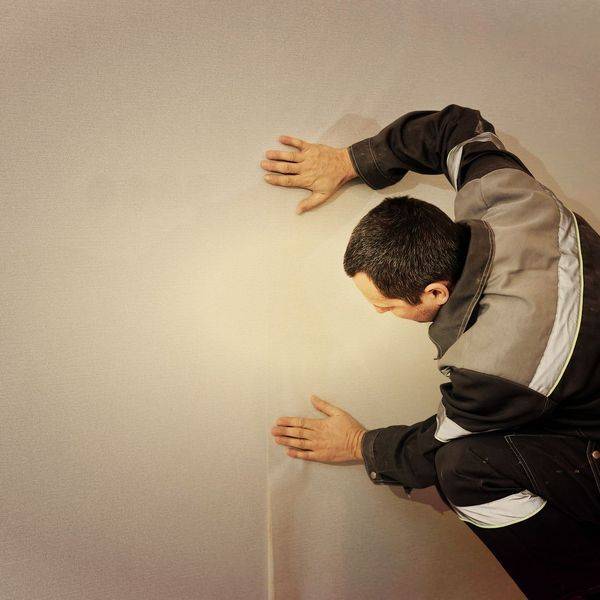 A man in a dark jacket works on a wall with both hands pressed to the surface.