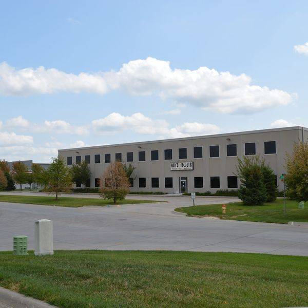 Low office building with a lawn, parking area and trees in front.