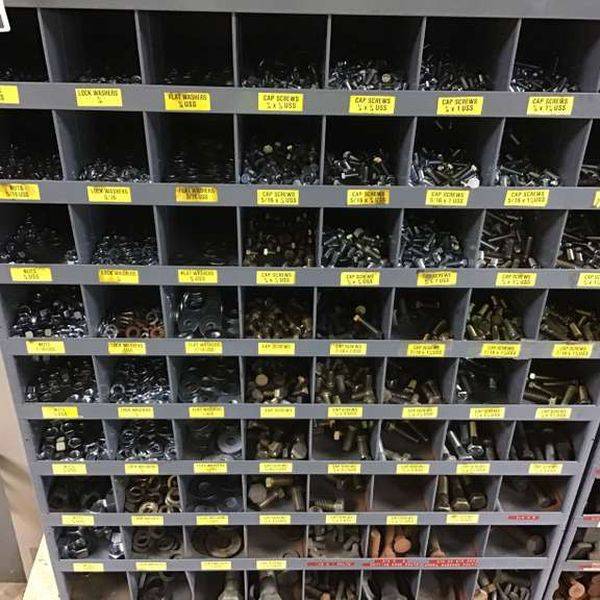 Wall of small metal parts bins, each labeled with a yellow tag.