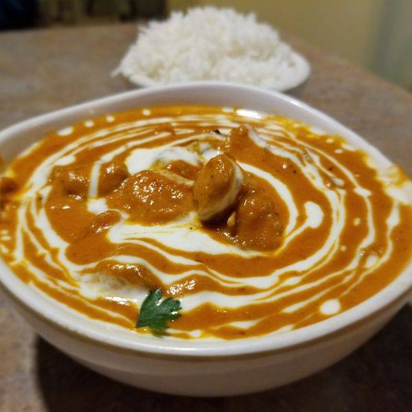 A bowl of creamy orange curry with a swirl of yogurt and a sprig of herb, served with rice.