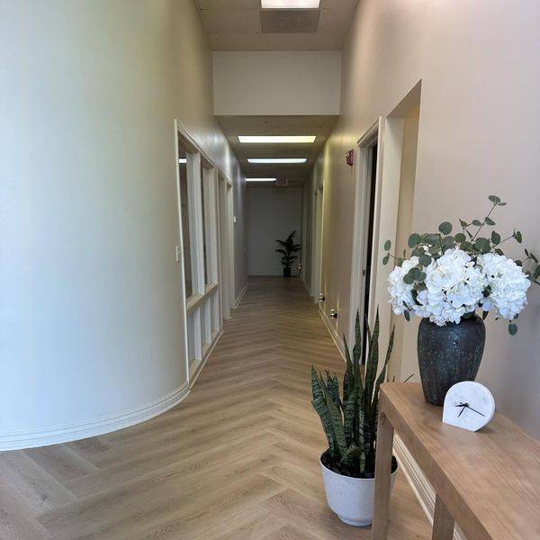 A bright hallway with herringbone wood floors, white flowers and a potted plant on a side table.