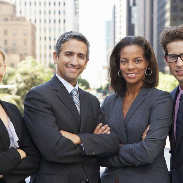 Three professionals in business attire smile together in a city setting.