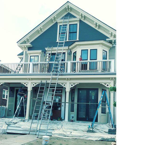 Blue house with ladders set up on its deck during exterior work.