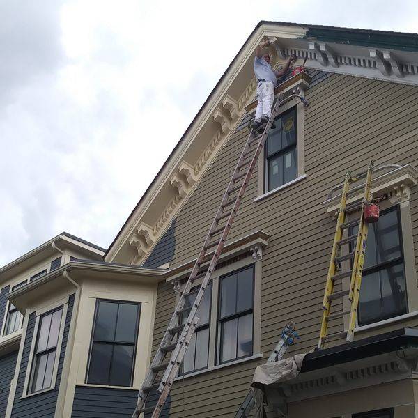 Tan house with two ladders leaning against its siding for exterior work.