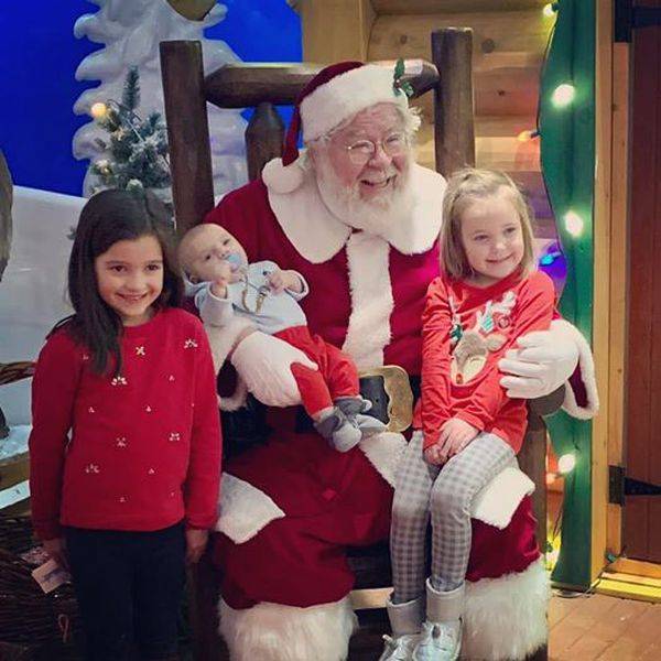 Santa seated with two young girls and a baby on his lap.