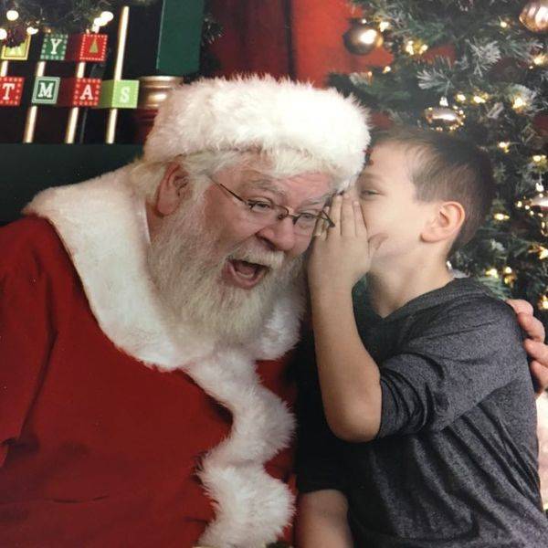 Santa leaning in to whisper to a young boy beside him.