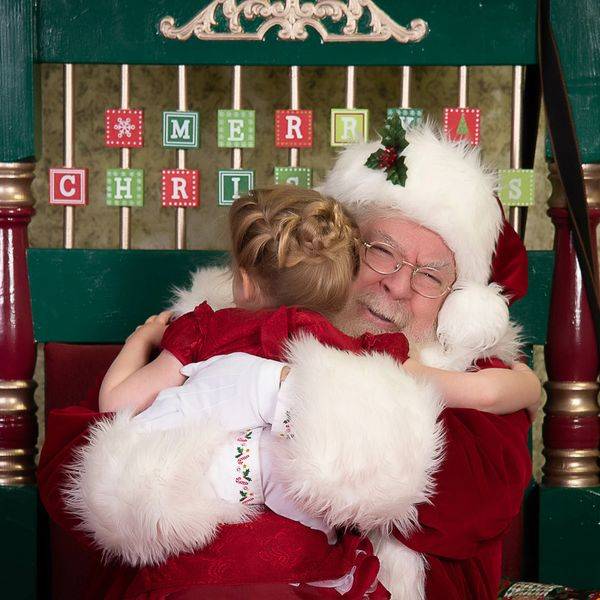 Child hugging Santa in a green chair decorated with holiday letters.