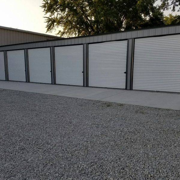 Metal storage buildings with white roll-up doors on a gravel drive.