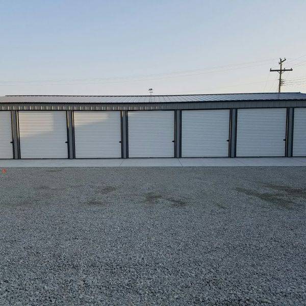 Straight-on view of a row of white storage unit doors beside a gravel lot.