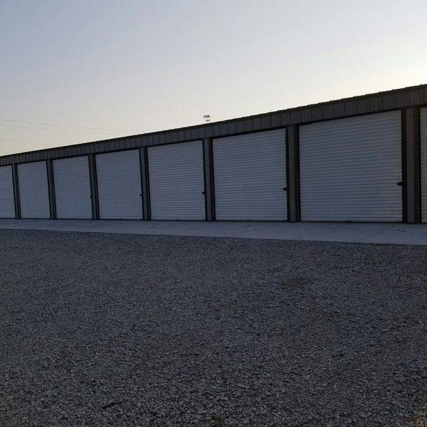 Angled view of a long row of white storage unit doors on a gravel lot.