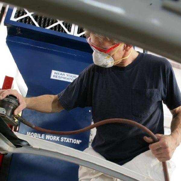 Technician wearing a respirator and using a power tool beside a mobile work station hood.