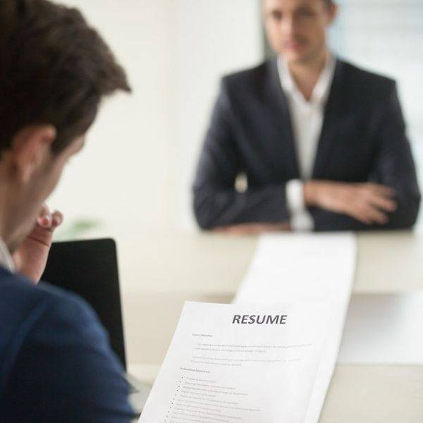 A printed resume on a table beside a candidate in a dark suit during an interview.