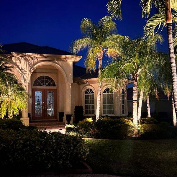 Home with palm trees and warm landscape lights at dusk.